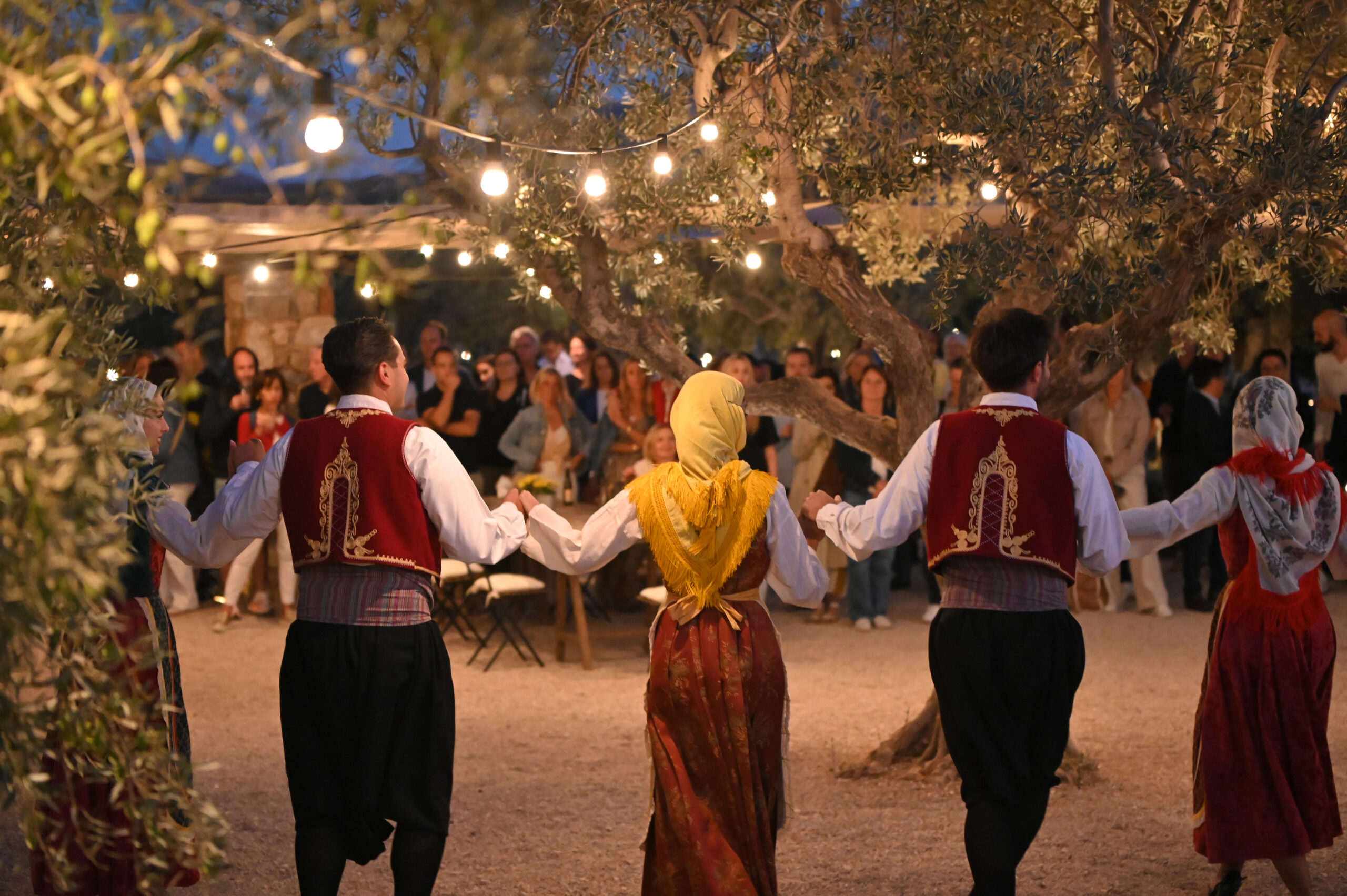 Nighttime outdoor dining scene with warmly lit glass pavilion and guests seated at tables
