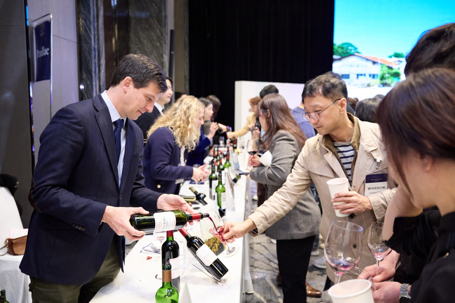 Man in suit pourng glass of red wine to another man for wine tasting event indoors