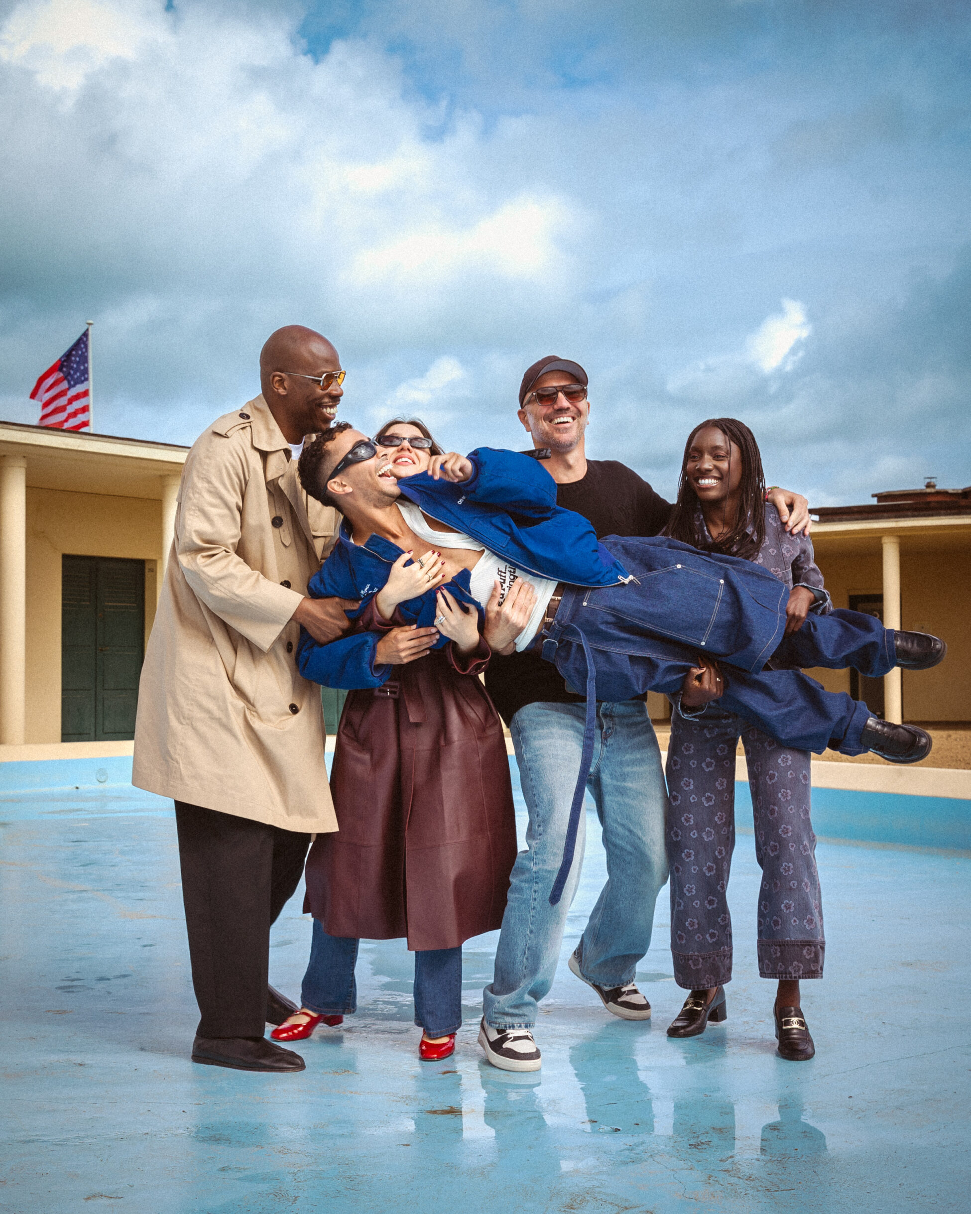 Group of happy friends lifting another person, laughing and smiling outdoors by empty pool