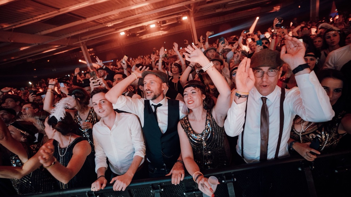 Enthusiastic crowd of people dressed in vintage attire dancing and cheering at lively event