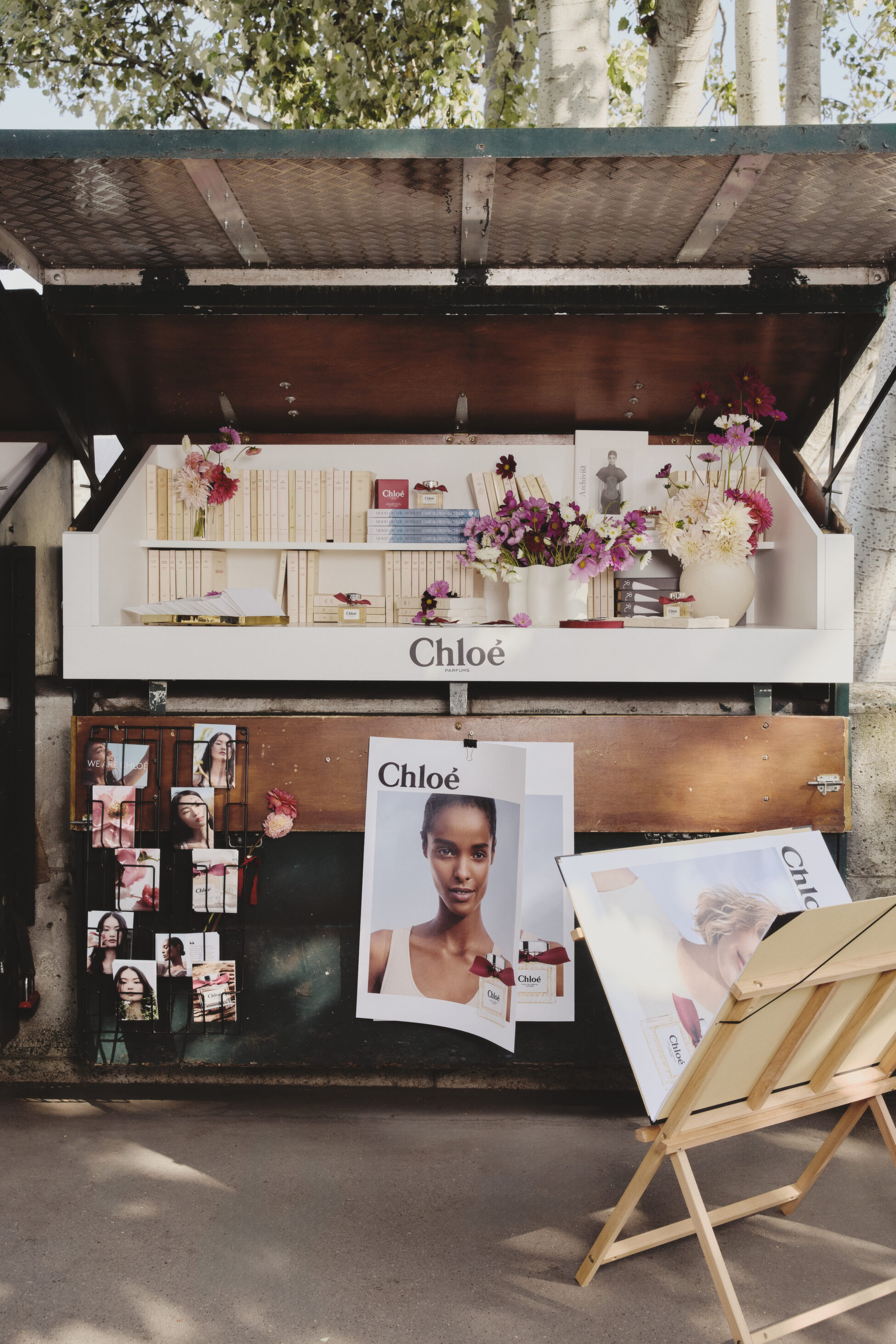 Chloé perfume display booth with floral arrangements, books, and promotional posters outdoors