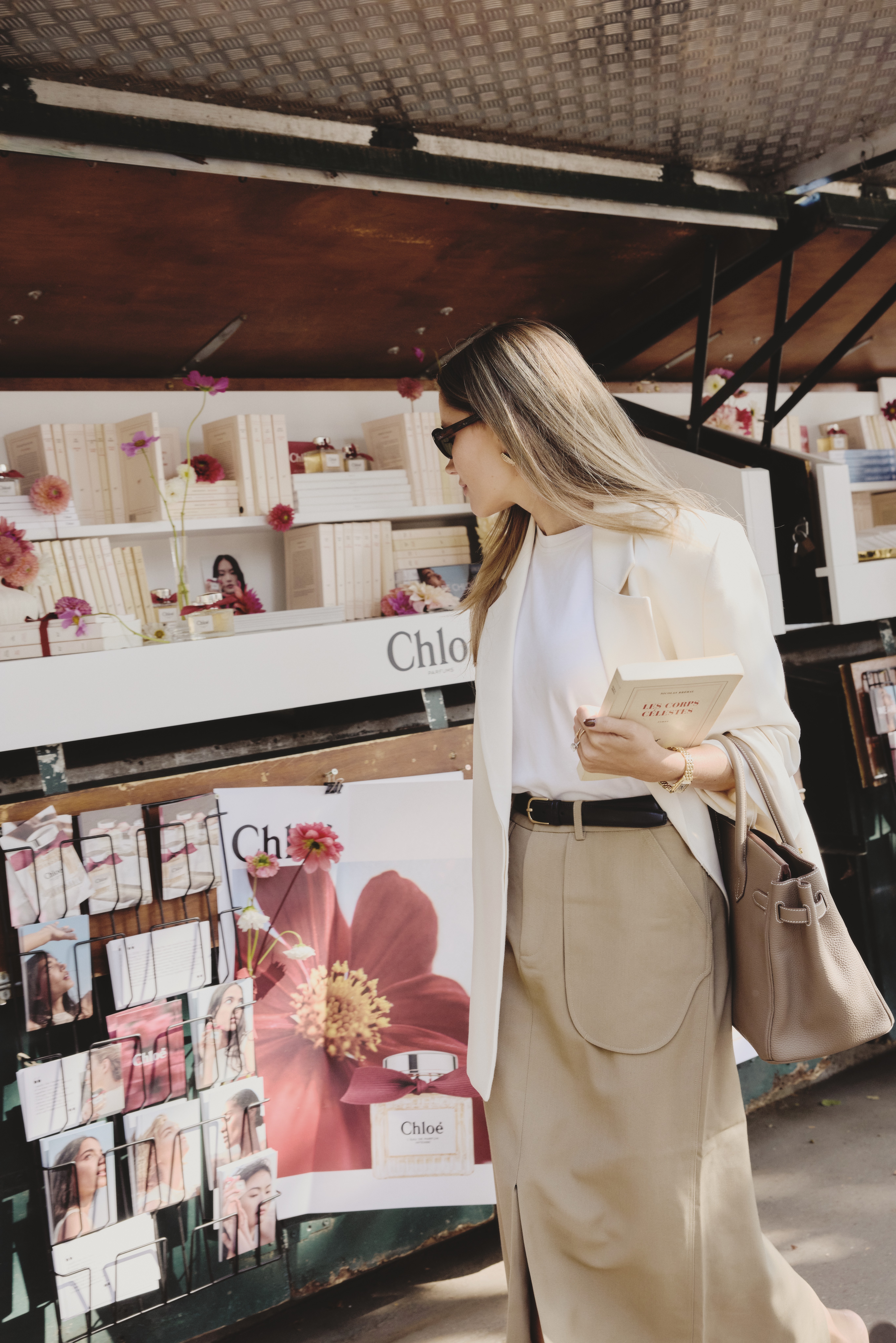 Woman in beige outfit browsing Chloé perfume and lifestyle display at outdoor market