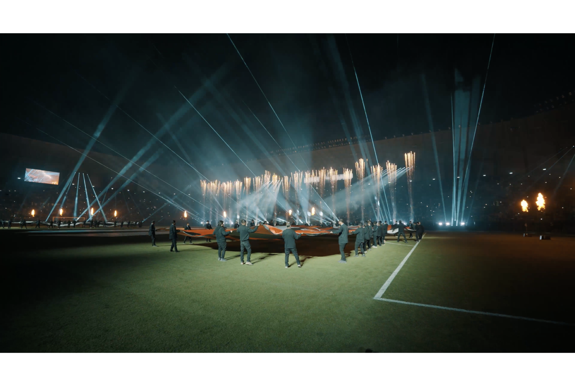 people holding huge flag in football stadium at night during ceremony